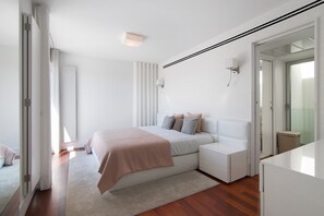 Un dormitorio moderno con cama, mesitas de noche, un velador y un gran ventanal, además de una puerta que da a otra habitación.