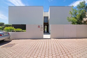 Un edificio moderno con entrada pavimentada, un coche estacionado afuera y un número de puerta visible.