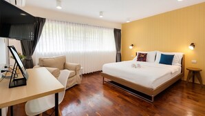 Moderni hotellihuone, jossa on puulattia, valkoisilla tekstiileillä varustettu sänky, työpöytä tietokoneella, tuoli ja televisio.