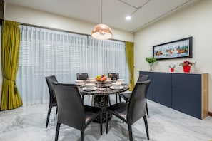 Un coin repas avec une table ronde, des chaises noires, un sol en marbre, un luminaire suspendu, un tableau au mur et un meuble orné de plantes.