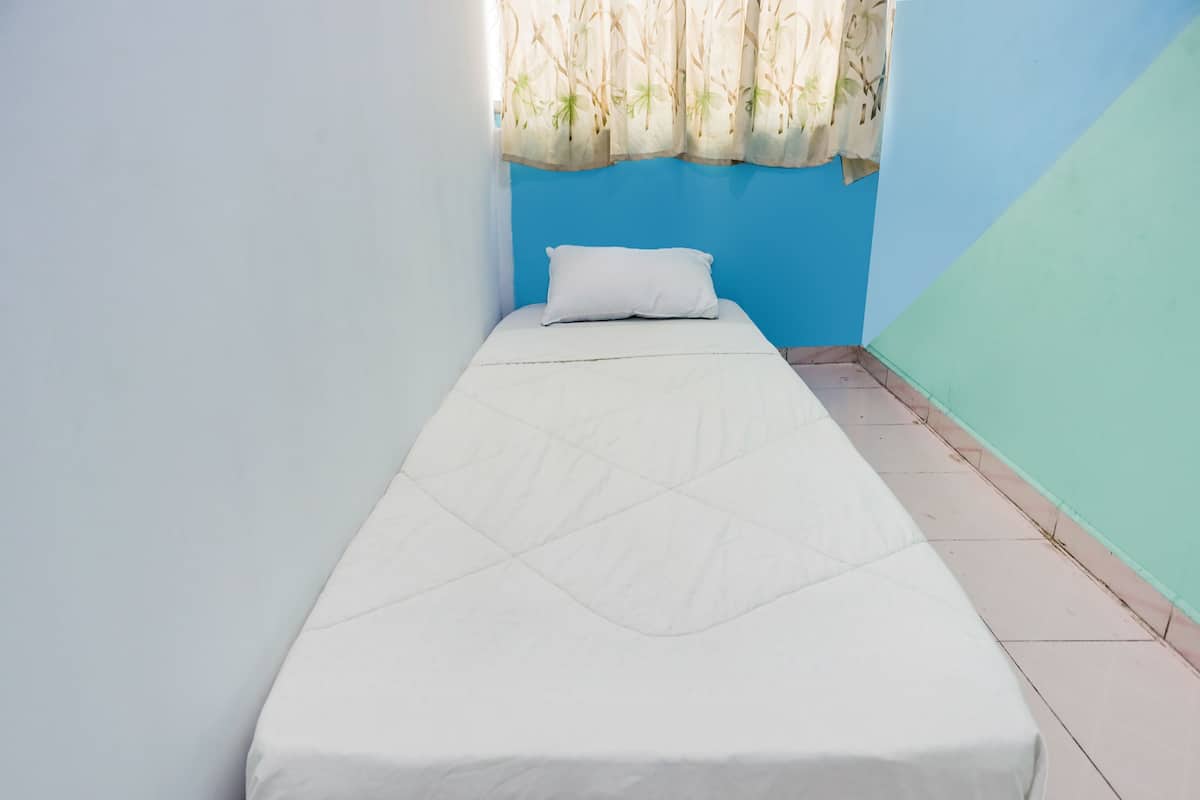 Una habitación pequeña con cama individual, pared azul y ventana con cortina estampada.