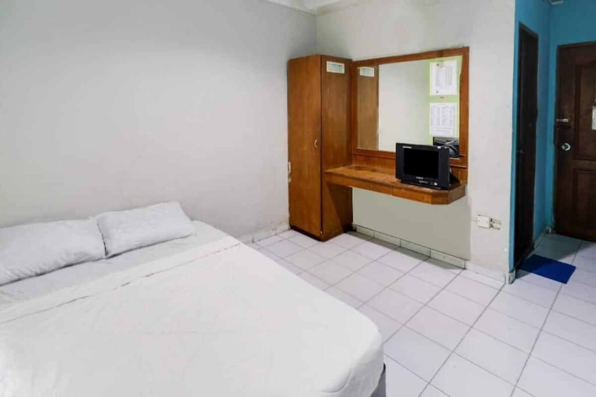Un dormitorio con una cama, un armario de madera, un escritorio pequeño con una computadora y una puerta.