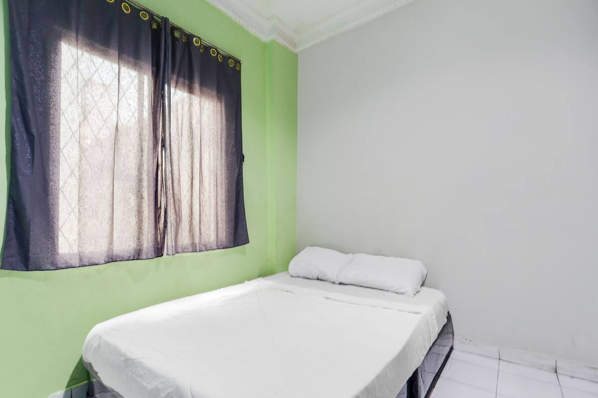 Una cama individual en una habitación con paredes verdes y una ventana con cortina.