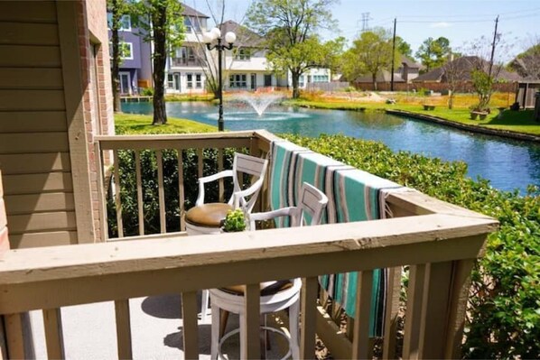 A balcony with a view of a canal, surrounded by greenery and residential buildings. - New renovated condo / lake view in Energy Corridor (Houston)