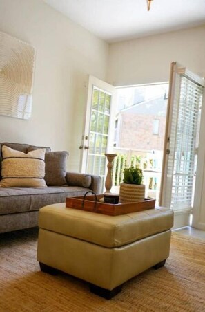 A living room with a sofa, an ottoman, a lamp, and a window with a view of a building. - New renovated condo / lake view in Energy Corridor (Houston)
