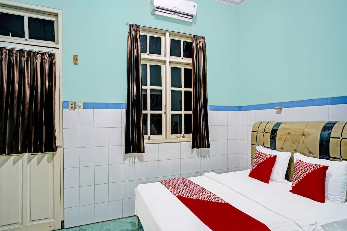 Une chambre d’hôtel avec un lit, une fenêtre avec des rideaux, un appareil de climatisation et un mur recouvert de carreaux.