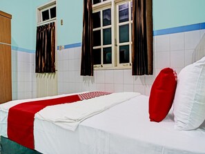 A bedroom with a bed, white and red bedding, a window with curtains, and a tiled wall.
