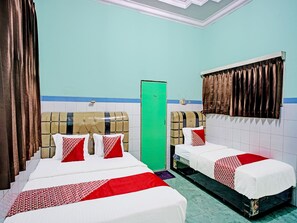 A hotel room with two beds, each with a patterned bedspread and pillows, a green door, and a window with curtains.