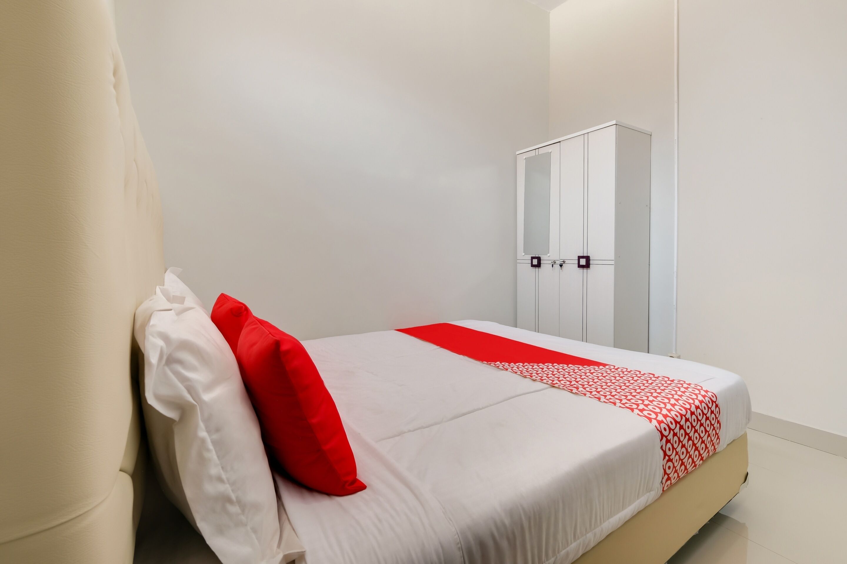 Ein ordentlich bezogenes Bett mit weißer und roter Bettwäsche, ein weißer Kleiderschrank und eine schlichte weiße Wand.