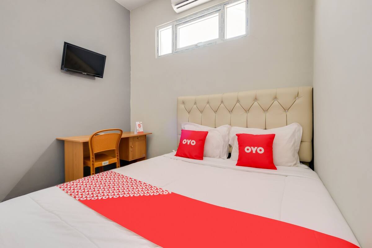 A hotel room with a bed, a desk, a chair, a television, and a window.