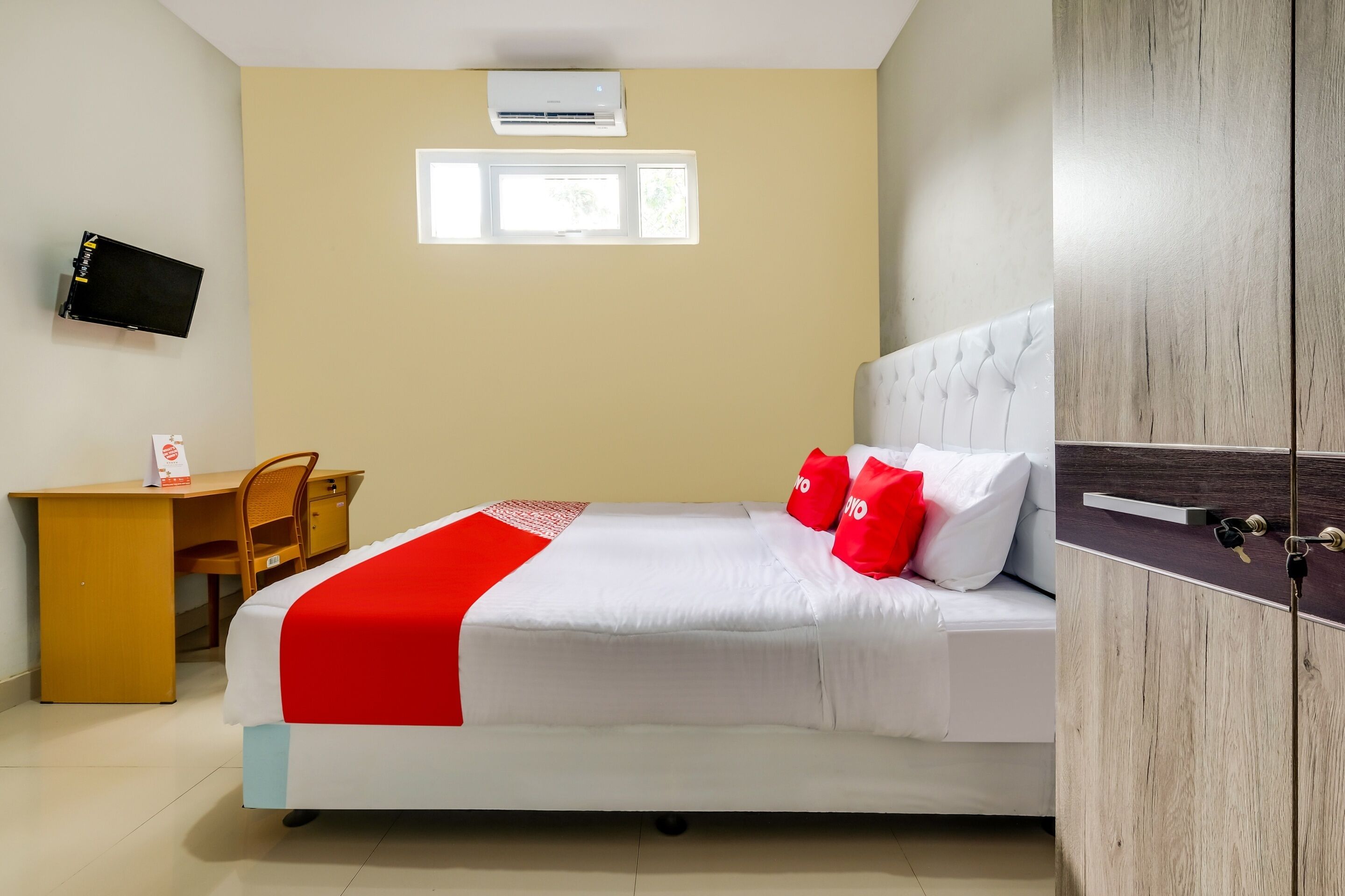 A hotel room with a bed, a desk, a chair, an air conditioner, and a television.