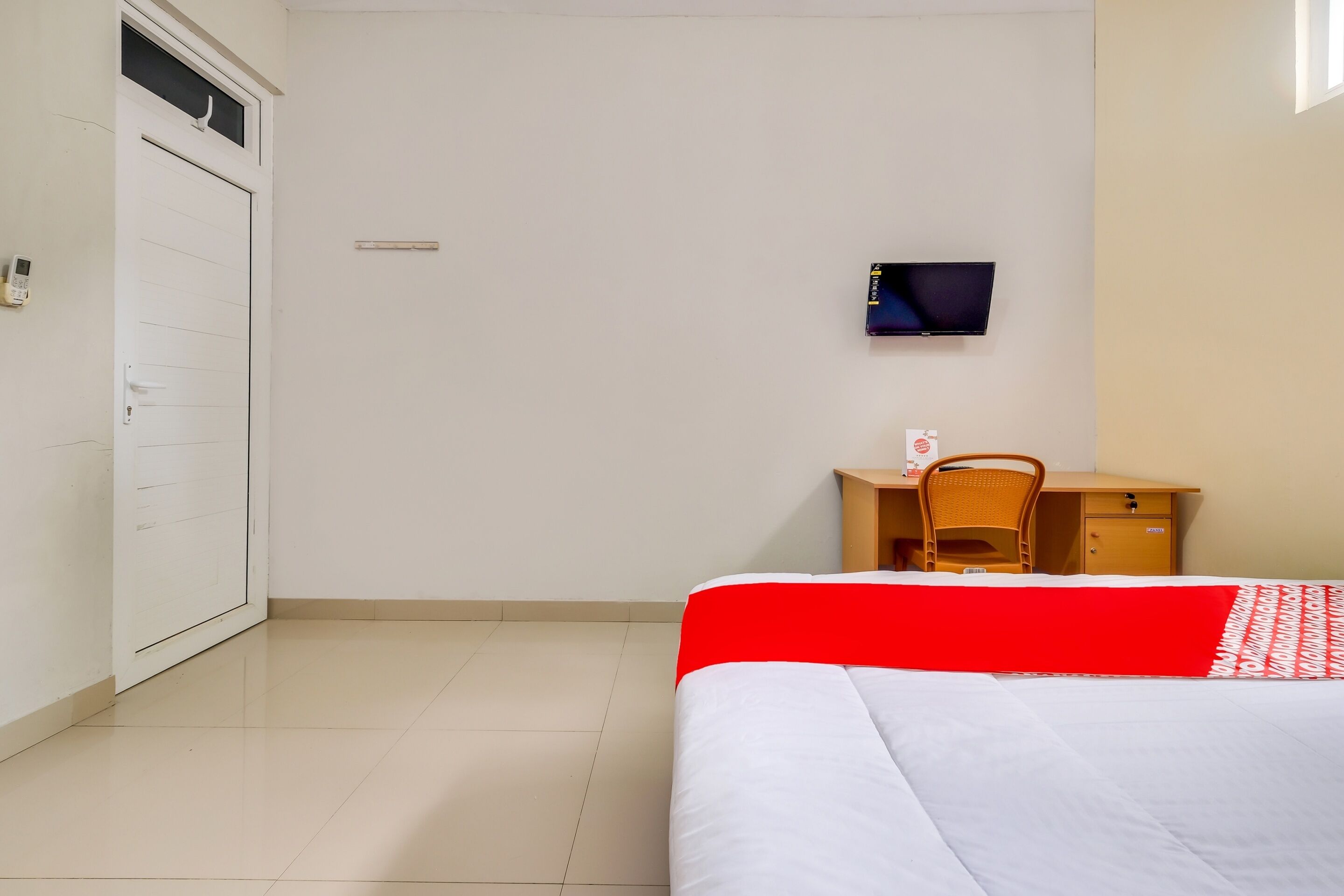 Habitación de hotel con cama, escritorio, silla, televisor y puerta.