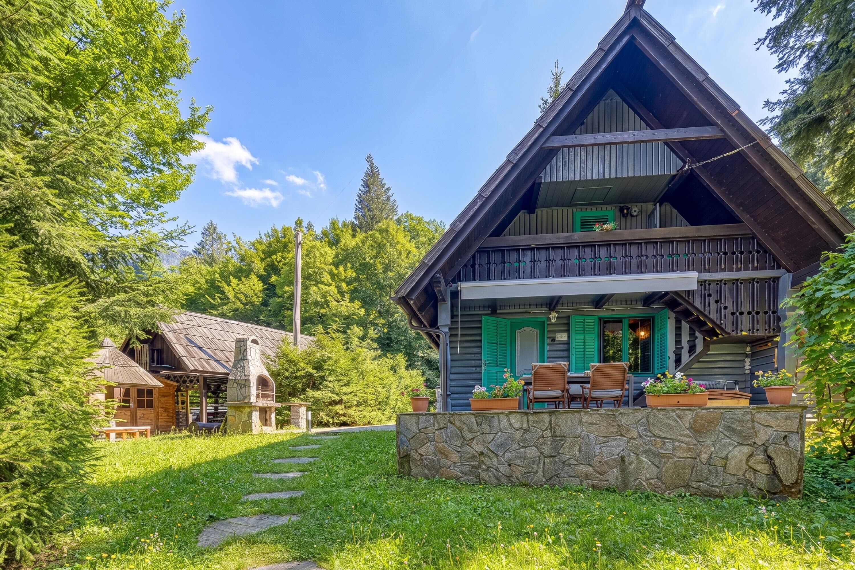 A two-story wooden cabin with a stone foundation, a balcony with chairs, and a stone wall in front.