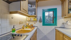 A compact kitchen with wooden cabinets, a sink, and a window with a teal frame.