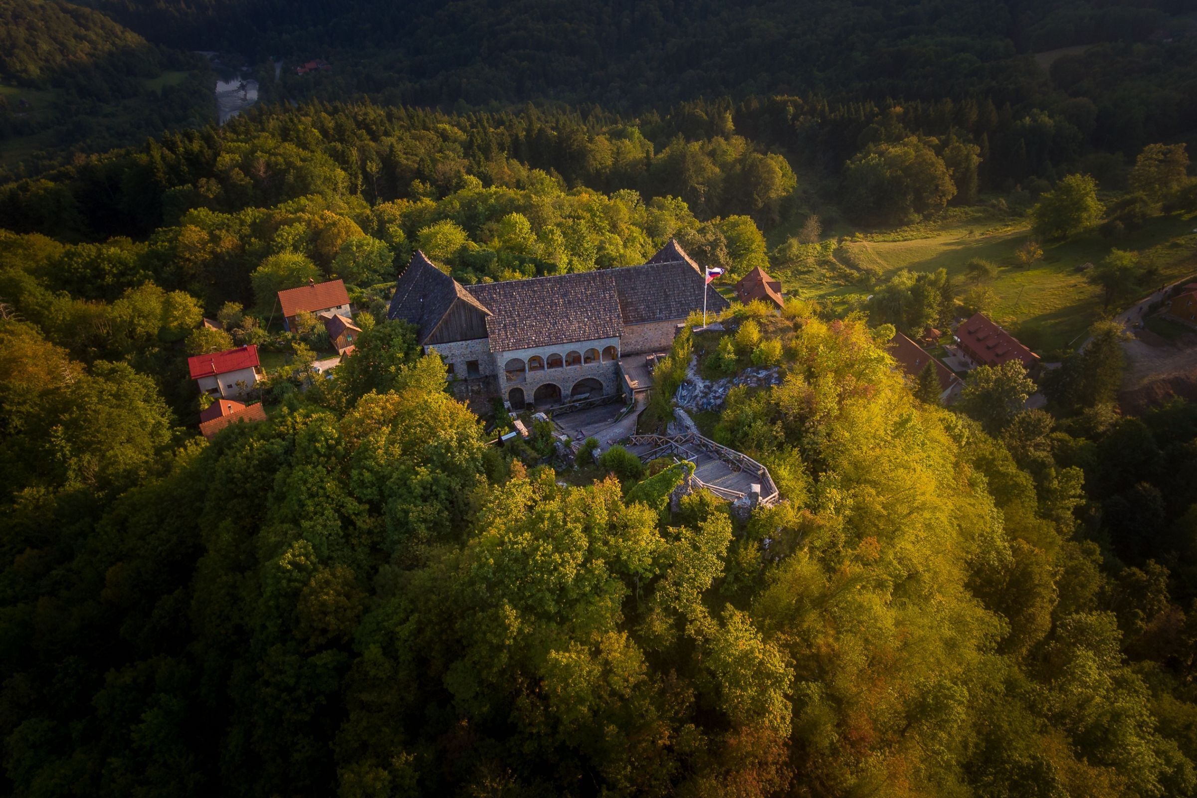 An aerial view of a historic building surrounded by dense forest, featuring a central courtyard and multiple buildings with red roofs.