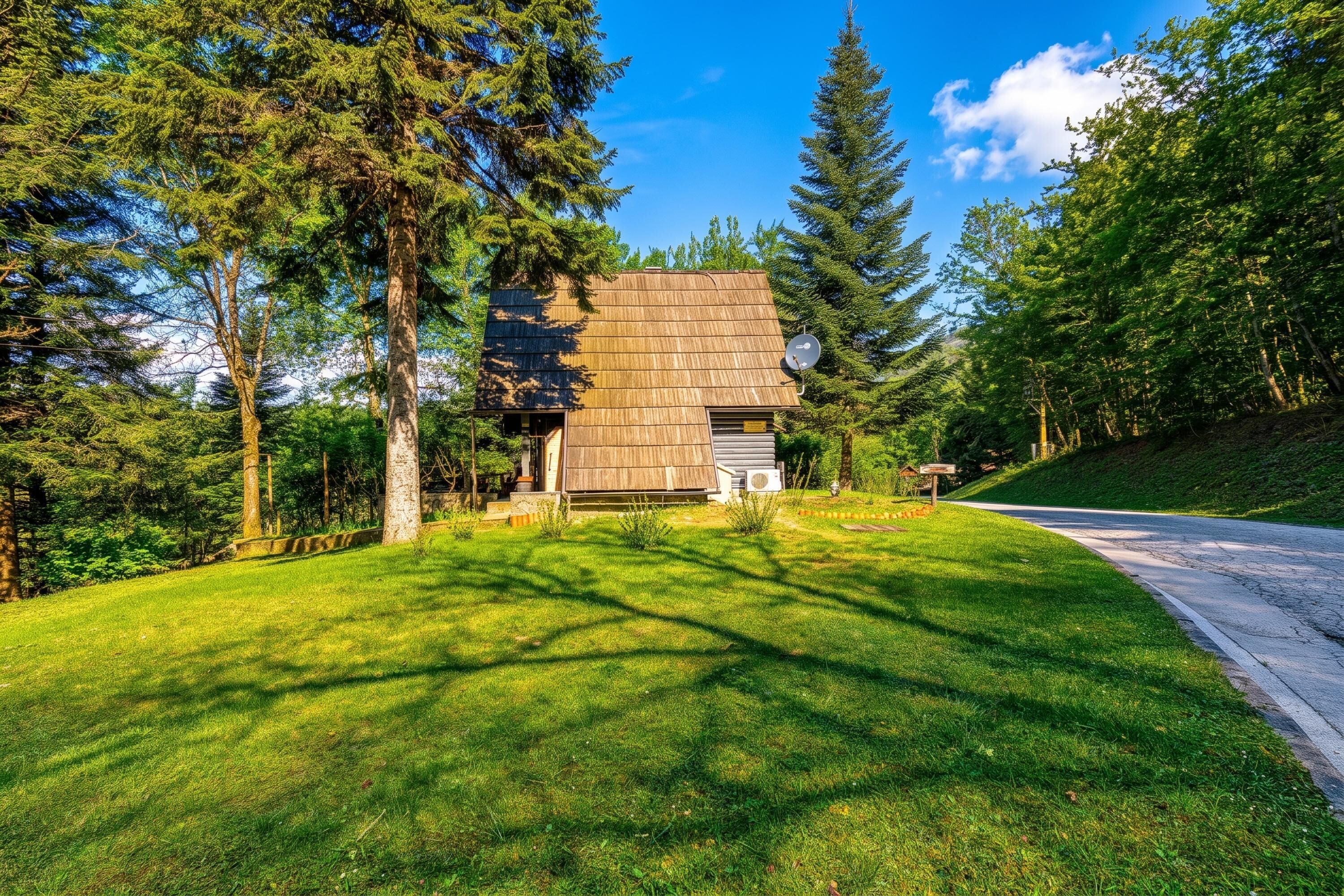 A rustic cabin with a sloped roof, surrounded by lush greenery and tall trees.