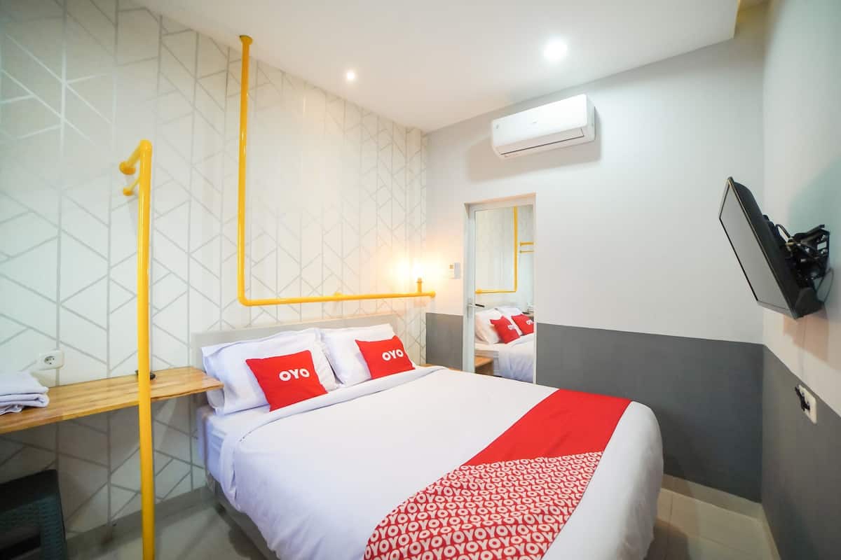 A hotel room with a bed, a nightstand, a mirror, and an air conditioning unit.