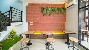A modern interior with a brick wall, green plants, and a seating area with wooden tables and stools. - Collection O Millenium Inn 2 (Medan)