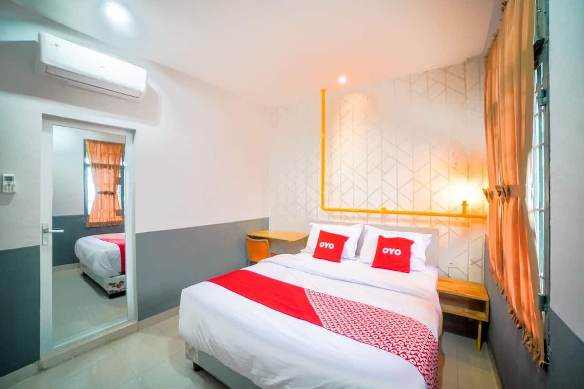 A hotel room with a bed, a bedside table, a mirror, and a window with curtains.