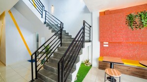 A modern interior with a staircase, a red brick wall, and a seating area with a wooden table and stool. - Collection O Millenium Inn 2 (Medan)