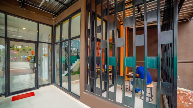 A modern interior with glass doors, a red mat at the entrance, and a seating area with green and blue chairs. - Collection O Millenium Inn 2 (Medan)