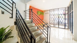 A staircase with black railings leading to a bright room with a red accent wall and a large window. - Collection O Millenium Inn 2 (Medan)