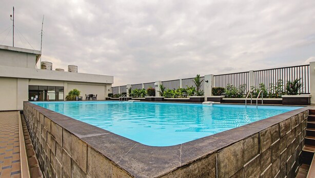 A rooftop swimming pool with a stone border, surrounded by a fence and potted plants. - Hotel O Tridasa (Medan)