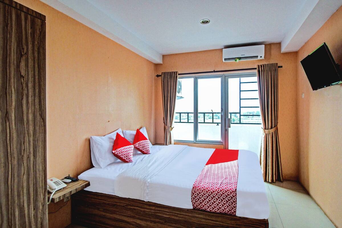 A hotel room with a bed, a bedside telephone, and a window with curtains.