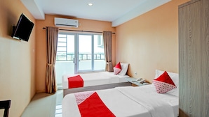 A hotel room with two beds, a TV mounted on the wall, an air conditioning unit, and a window with curtains. - Hotel O Tridasa (Medan)