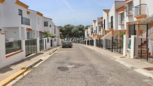 En boligvej med hvide huse, altaner og en parkeret bil.
