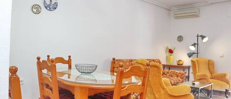 Un comedor con una mesa redonda de vidrio, sillas de madera y un sillón amarillo.