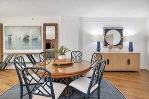 A dining area with a round table, six chairs, a cabinet, and two wall-mounted lamps. - Oceanfront Condo Pool Hot tub Private Beach Access (Saint Simons Island)
