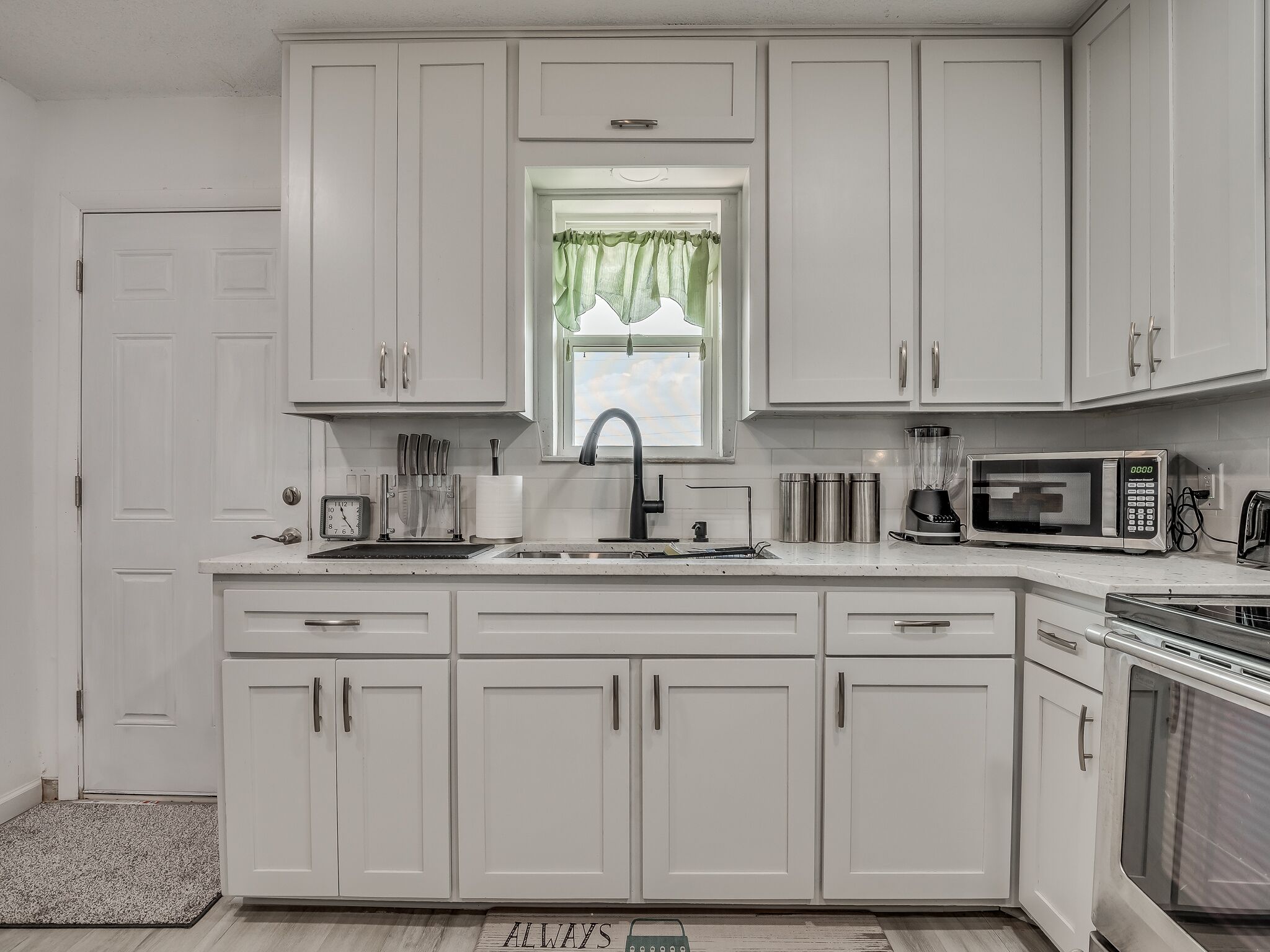 Una cocina moderna con armarios blancos, un lavamanos de acero inoxidable, un microondas y un tostador.