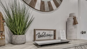 A reception desk with a 'Welcome' sign, a potted plant, a decorative wall piece, and a cylindrical container with a tassel. - Capital View - Downtown OKC 7 MINS AWAY (Oklahoma City)