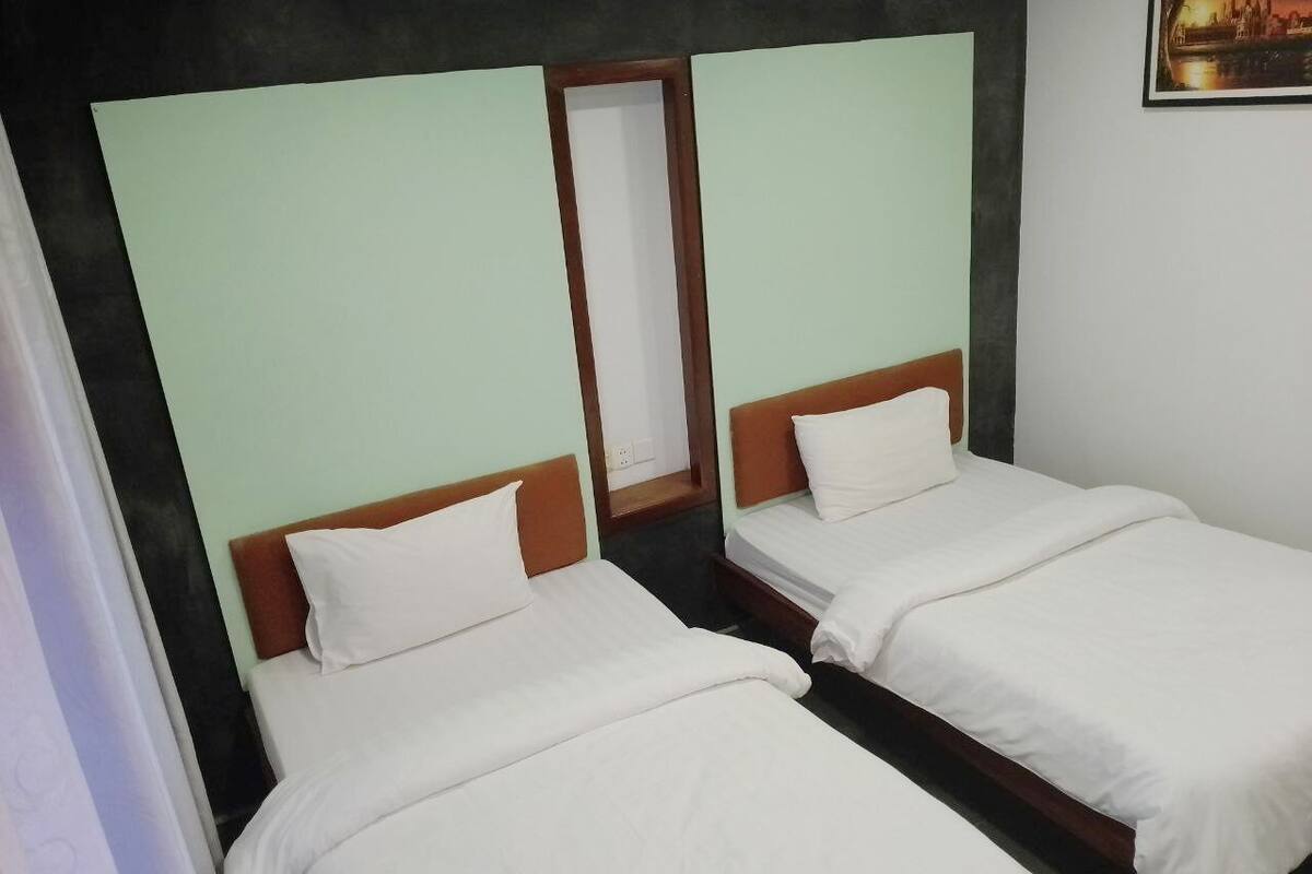 A room with two single beds, each with a wooden headboard and white bedding.