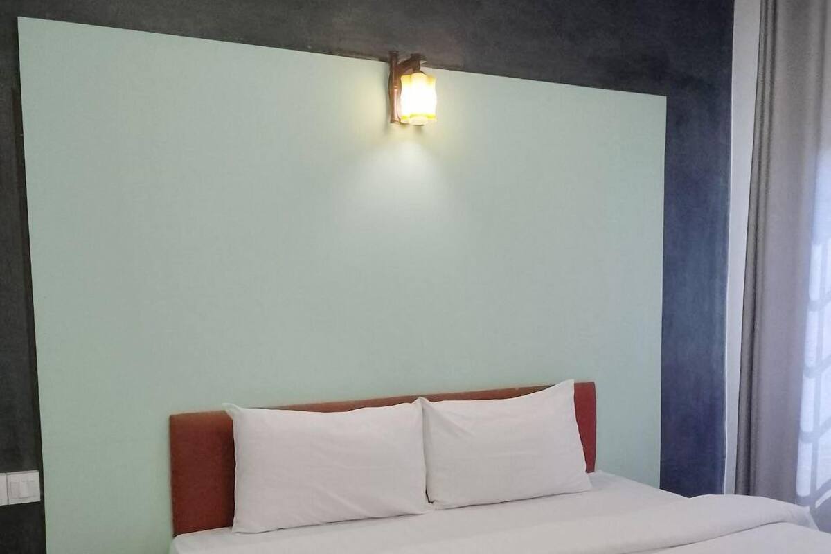 A hotel room with a bed, a nightstand, a wall-mounted light, and a window with curtains.