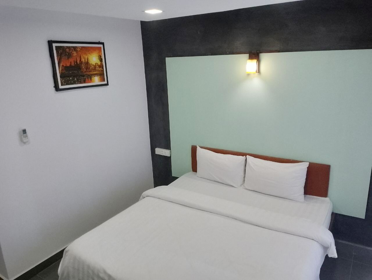 A hotel room with a bed, a wall-mounted picture, and a light fixture.