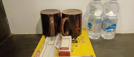 Una mesa con un libro, dos tazas de café, dos botellas de agua, un hisopo, un botiquín de primeros auxilios y un paquete de cuidado.