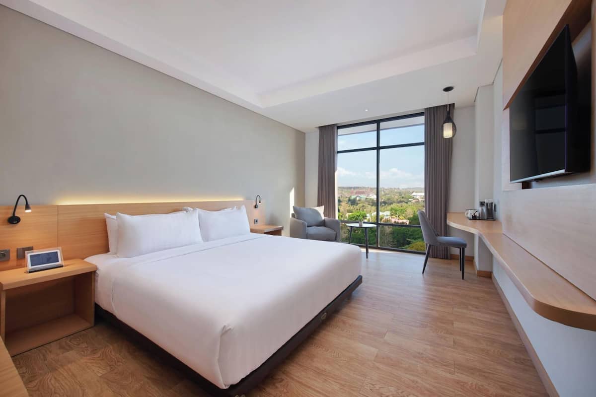 A modern hotel room with a large bed, a desk, a TV, and a view of the city.