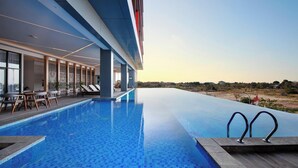 A modern hotel with a large infinity pool, lounge area, and a view of the landscape.