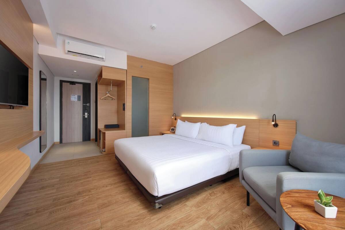 A modern hotel room with a large bed, a sofa, a small table with a plant, and a TV mounted on the wall.