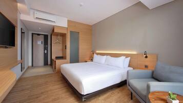 A modern hotel room with a large bed, a sofa, a small table with a plant, and a TV mounted on the wall.