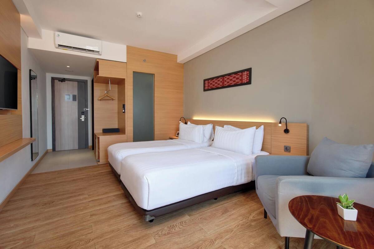 A modern hotel room with a large bed, a sofa, a small table with a plant, and a TV mounted on the wall.