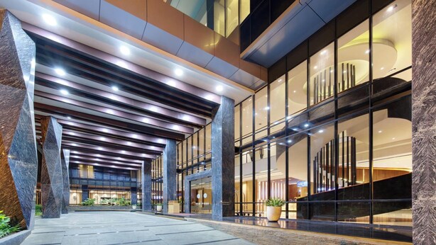 A modern hotel entrance with a covered walkway, large glass windows, and a central marble column.