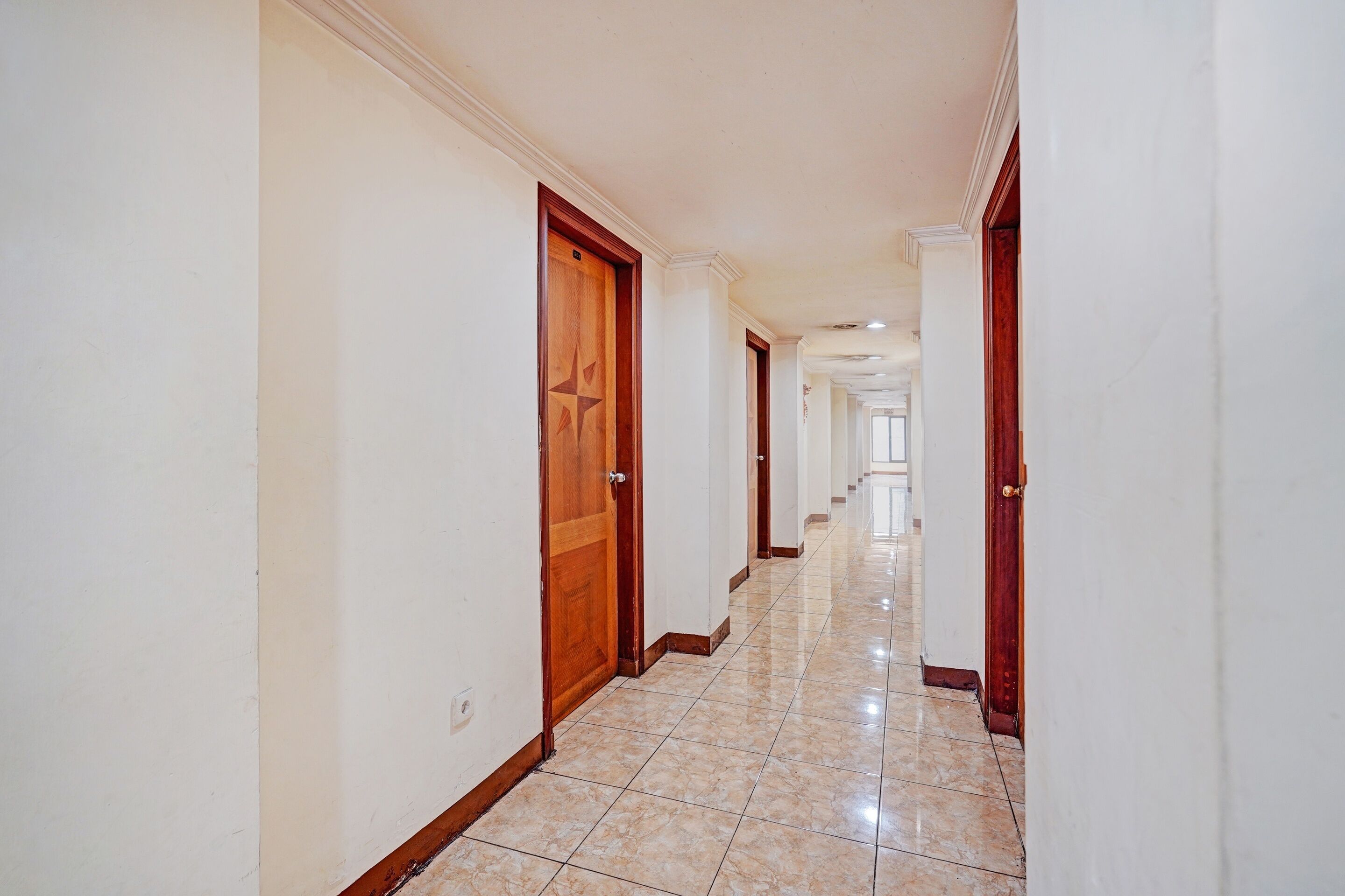 Un pasillo con puertas a ambos lados que conduce a una habitación luminosa al final.