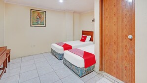A hotel room with two beds, a wooden desk, a painting on the wall, and a wooden door. - OYO Life 90380 Andalus Hotel Syariah (Surabaya)