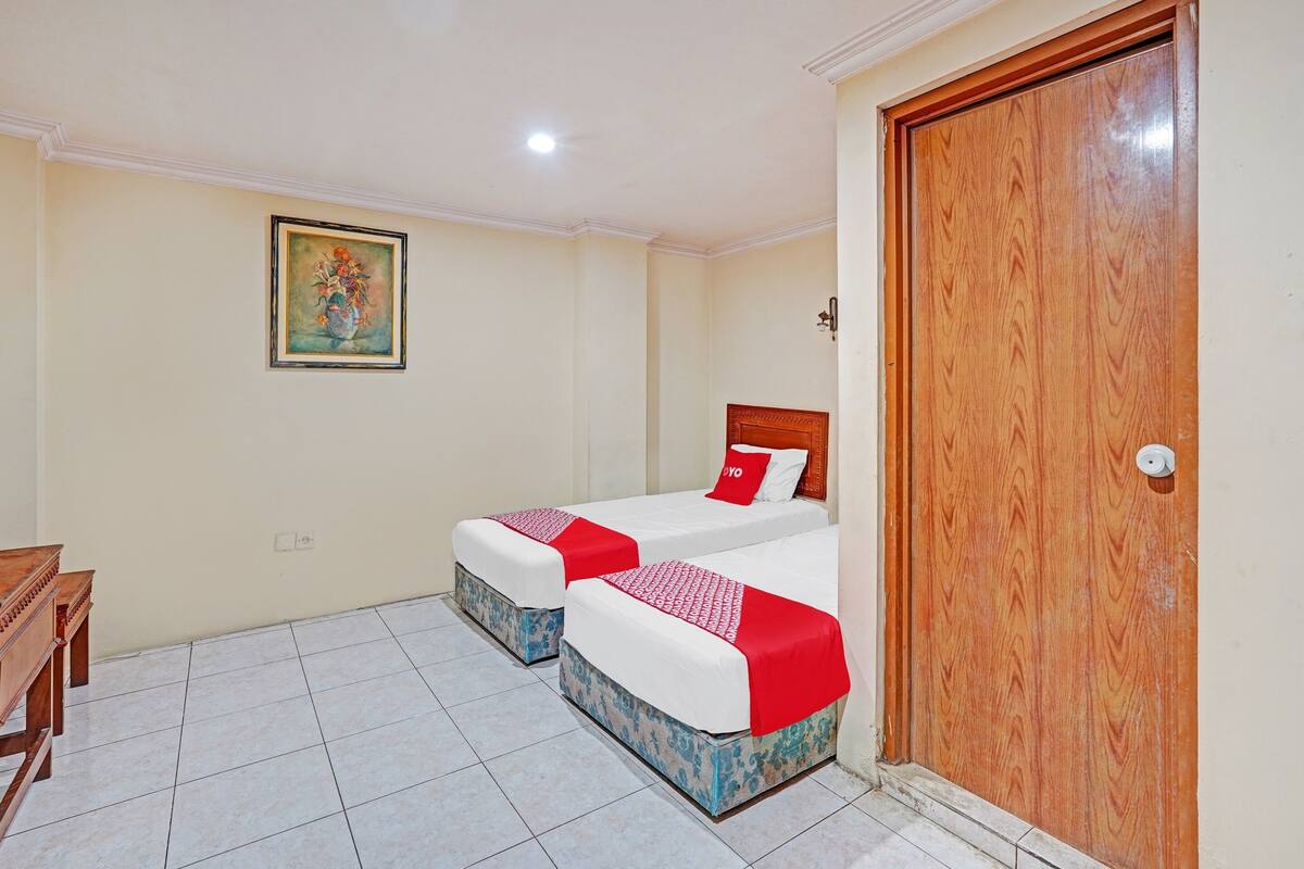 A hotel room with two beds, a wooden desk, a painting on the wall, and a wooden door.