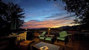 An outdoor seating area with chairs and tables, overlooking a sunset with mountains in the distance.