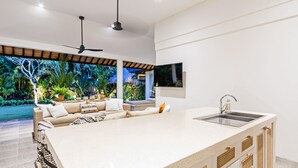 A modern kitchen with a large island, a built-in sink, and a ceiling fan. - Baliani Beauty (Seminyak)