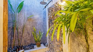 A small, enclosed outdoor shower area with a stone wall, a potted plant, and a bamboo plant. - Baliani Beauty (Seminyak)